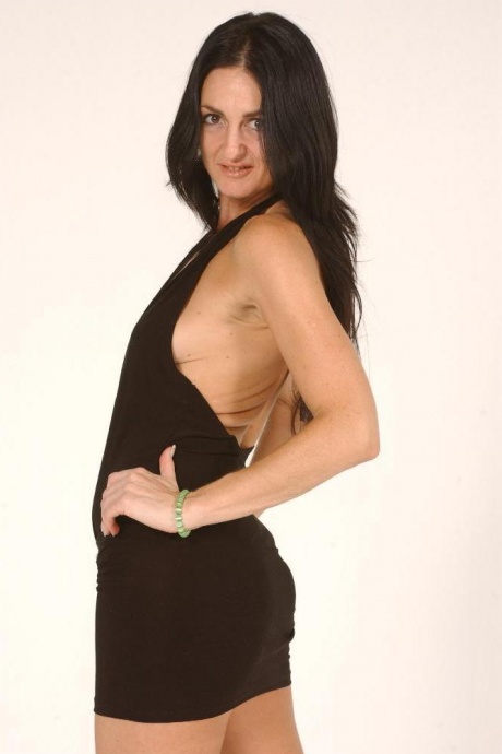 Темноволосая женщина моделирует короткое платье перед тем, как надеть страпон на член 3